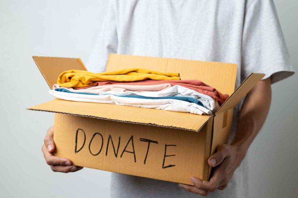 Donation Concept, man holding clothes with donate box in white background room.