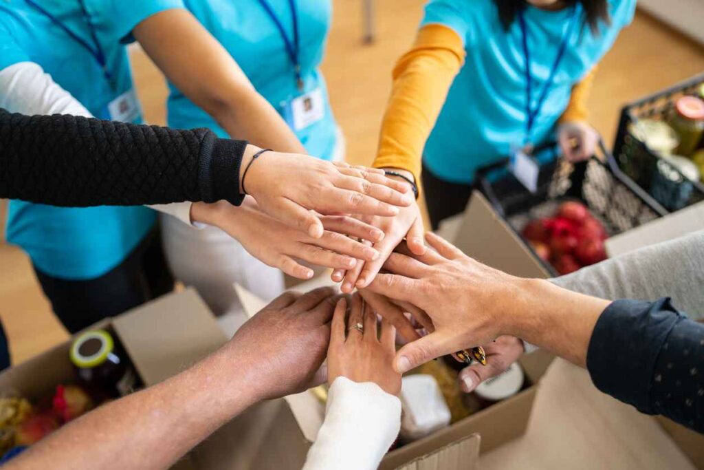 A group of charity workers hands stacked into a circle for unity, over boxes of groceries; Giving Back as a New Year's Resolution