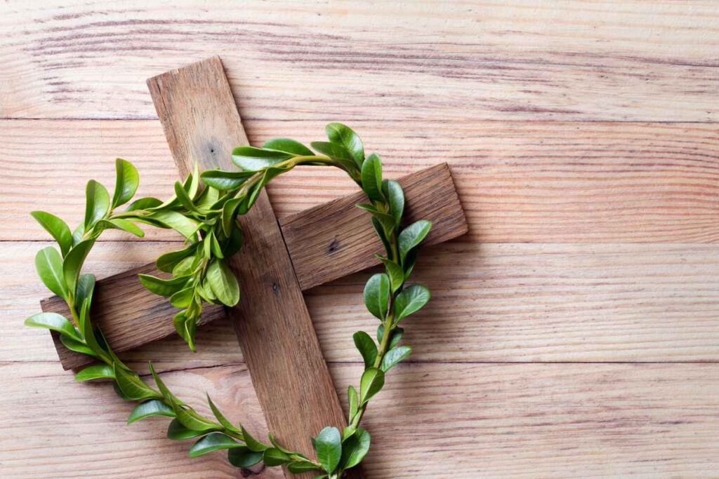 Wooden cross with sprigs of boxwood in heart-shaped, easter symbol of life, religious concept background