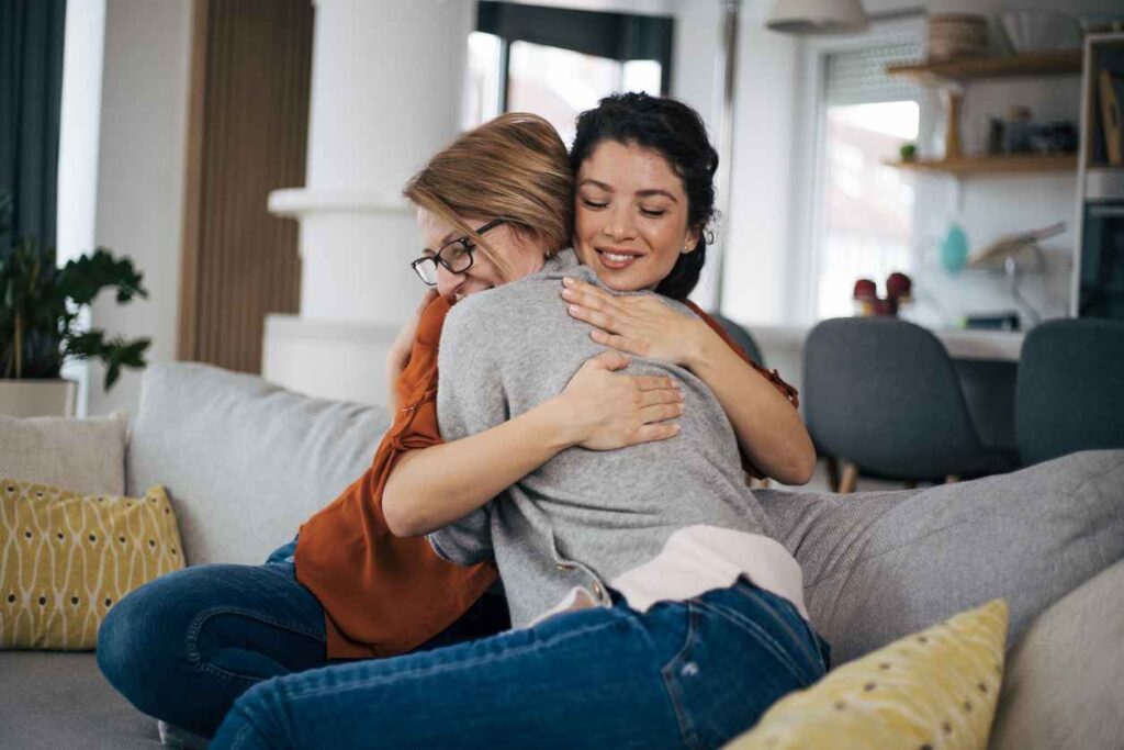 Happy mother and daughter embracing each other at home on sofa.